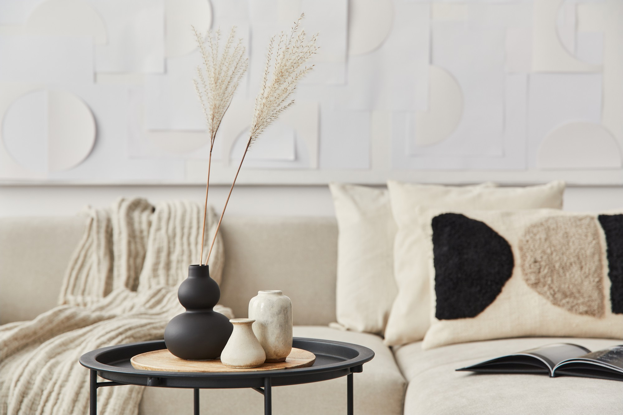 Composición elegante en un interior elegante con mesa de centro de madera, flores secas en jarrón, almohada, manta, pinturas de arte y libro en la decoración del hogar moderno.